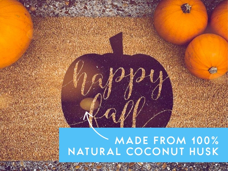 Puede incluir: Una alfombra de bienvenida marr&oacute;n con una silueta de calabaza negra que dice "happy fall" en purpurina dorada. La alfombra est&aacute; hecha de 100% fibra de coco natural. Hay tres calabazas naranjas en la esquina superior derecha de la alfombra.