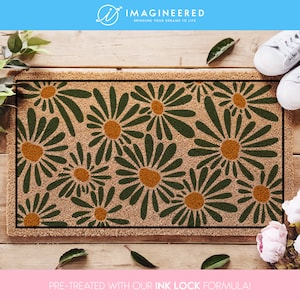 May include: A brown coir doormat with a green and orange daisy pattern. The text "PRE-TREATED WITH OUR INK LOCK FORMULA!" is printed on the bottom of the mat.