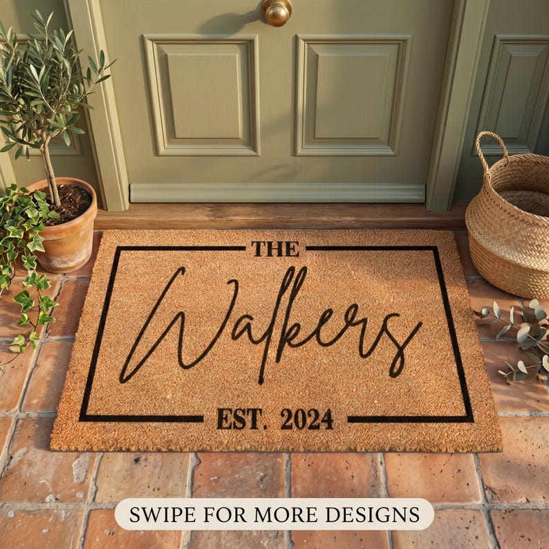 May include: A rectangular coir doormat with a black border and the text "THE Walkers EST. 2024" in a cursive font. The mat is placed in front of a green door, with a potted plant and a woven basket nearby.