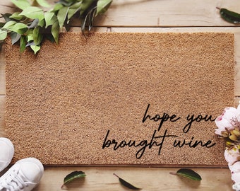 May include: A brown coir doormat with the text "hope you brought wine" in black cursive lettering. The doormat is pre-treated with an ink lock formula.