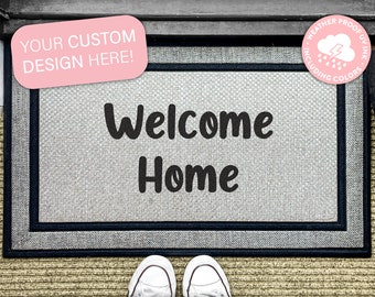 Puede incluir: Una alfombra de bienvenida gris con ribete negro y el texto "Welcome Home" en negro. La alfombra es resistente a la intemperie y tiene un área de diseño personalizado. El texto "YOUR CUSTOM DESIGN HERE!" está en un cuadro rosa.