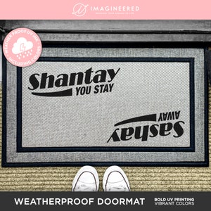 May include: Weatherproof doormat with the text "Shantay You Stay" and "Saseay Away" in black lettering on a gray background.