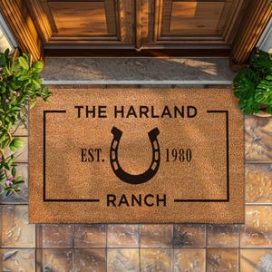 Op de afbeelding: Een bruine kokosvezel deurmat met de tekst "THE HARLAND RANCH EST. 1980" in een zwarte rechthoek met een hoefijzer in het midden.
