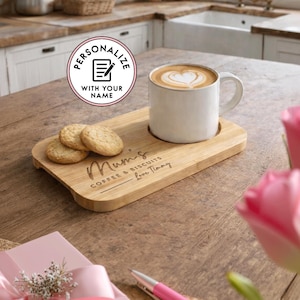 May include: A wooden serving tray with a white mug of coffee and three cookies. The tray has the words "Mum's Coffee & Biscuits Love Timmy" engraved on it. A pink pen and flowers are in the foreground.