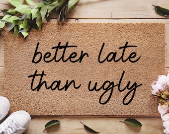 May include: A brown coir doormat with the text "better late than ugly" in black lettering. The doormat is pre-treated with an ink lock formula.