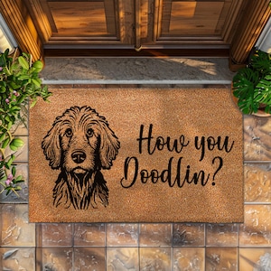May include: A brown coir doormat with the text "How you Doodlin?" in black lettering. A black and white illustration of a doodle dog is on the left side of the mat.
