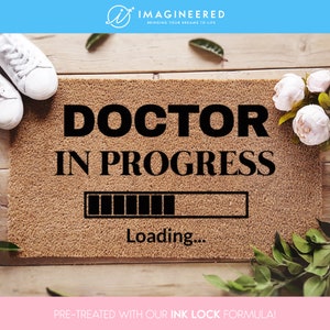 May include: A brown doormat with the text "DOCTOR IN PROGRESS" and a loading bar graphic. The text "Loading..." is below the bar. The doormat is pre-treated with an ink lock formula.