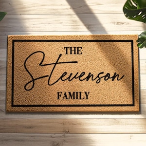May include: A rectangular doormat with a textured, tan surface and a black border. The mat features the words "THE Stevenson FAMILY" in a stylish, black script font, making it a personalized home decor item.