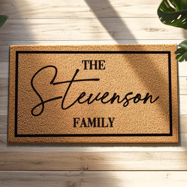 May include: A rectangular doormat with a textured, tan surface and a black border. The mat features the words "THE Stevenson FAMILY" in a stylish, black script font, making it a personalized home decor item.