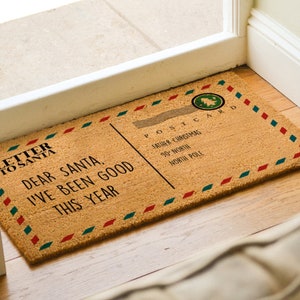 Puede incluir: Una alfombra de coco marr&oacute;n con un borde rojo, blanco y azul. La alfombra tiene un dise&ntilde;o de postal vintage con el texto "Carta a Pap&aacute; Noel" y "Querido Pap&aacute; Noel, he sido bueno este a&ntilde;o". La postal tambi&eacute;n tiene el texto "Postal Pap&aacute; Noel 90 Norte Polo Norte".