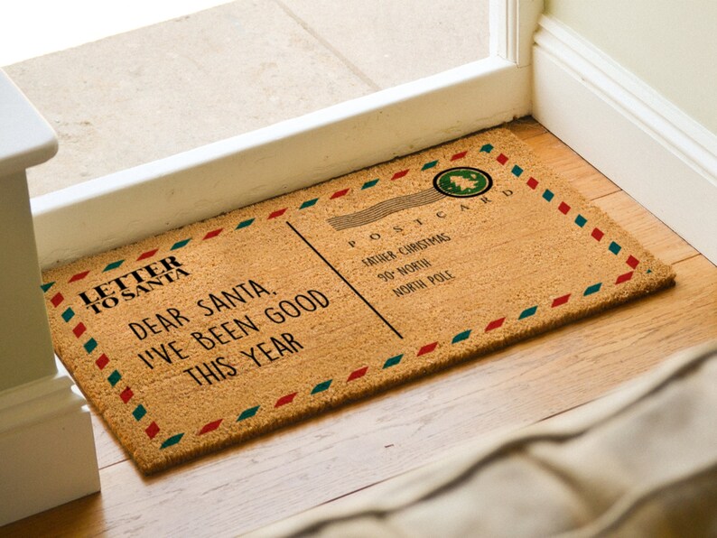 Puede incluir: Una alfombra de coco marr&oacute;n con un borde rojo, blanco y azul. La alfombra tiene un dise&ntilde;o de postal vintage con el texto "Carta a Pap&aacute; Noel" y "Querido Pap&aacute; Noel, he sido bueno este a&ntilde;o". La postal tambi&eacute;n tiene el texto "Postal Pap&aacute; Noel 90 Norte Polo Norte".