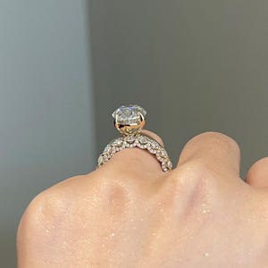 May include: A gold engagement ring with a large, clear, round-cut diamond. The band features a delicate, ornate design with smaller accent stones. The ring is shown on a hand, showcasing its sparkle and intricate details.