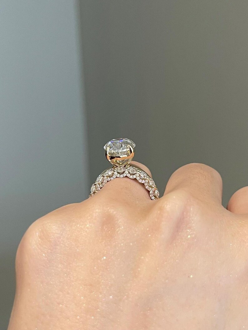 May include: A gold engagement ring with a large, clear, round-cut diamond. The band features a delicate, ornate design with smaller accent stones. The ring is shown on a hand, showcasing its sparkle and intricate details.