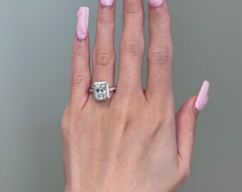Puede incluir: Una mano con esmalte de uñas rosa y un gran anillo de compromiso de diamantes.