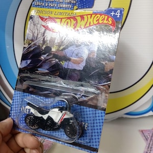 May include: A Hot Wheels toy motorcycle in a clear plastic package. The motorcycle is white with black wheels and red and black accents. The packaging has the words "EDICIÓN LIMITADA" and "+4" printed on it.