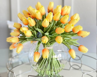 May include: A bouquet of yellow and orange tulips in a clear glass vase. The vase is sitting on a silver tray with a mirrored surface.