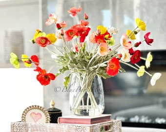 May include: A bouquet of red, yellow and white poppy flowers in a clear glass vase on a white wooden tray with a book and a decorative heart-shaped box. The flowers are arranged in a vase on a white wooden tray with a book and a decorative heart-shaped box.