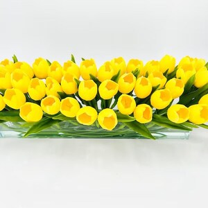May include: A glass vase filled with a large arrangement of yellow artificial tulips.