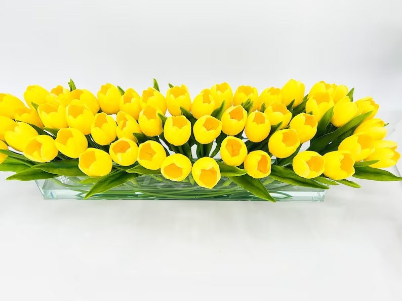 May include: A glass vase filled with a large arrangement of yellow artificial tulips.