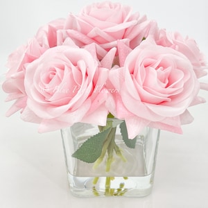 May include: A bouquet of pink silk roses arranged in a clear glass vase. The roses are in full bloom and have a soft, delicate appearance.