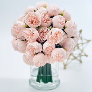 May include: A bouquet of blush pink silk peonies arranged in a clear glass vase. The vase has a textured base.