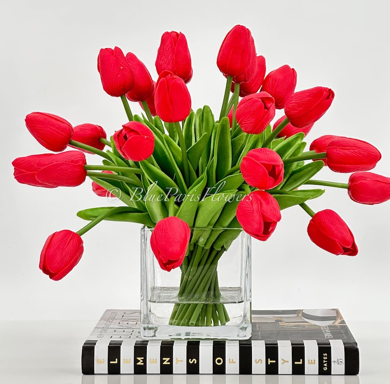 May include: A bouquet of red tulips arranged in a clear glass vase. The vase is sitting on a black and white striped surface.
