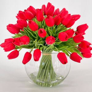 May include: A bouquet of red tulips arranged in a clear glass vase. The tulips are artificial and have green stems.