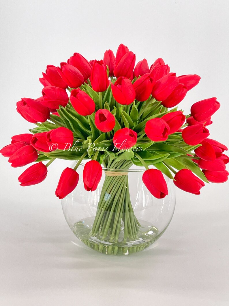 May include: A bouquet of red tulips arranged in a clear glass vase. The tulips are artificial and have green stems.