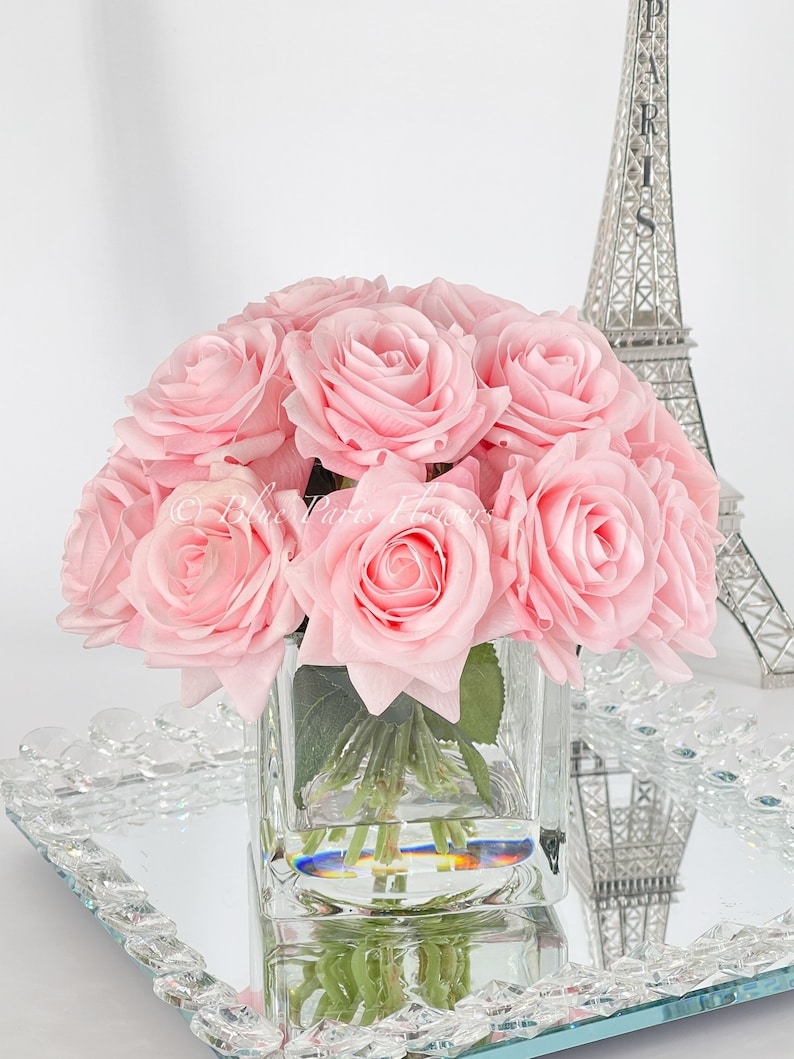 May include: A bouquet of pink silk roses in a clear glass cube vase, sitting on a mirrored tray with a silver Eiffel Tower in the background.