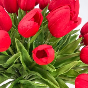 May include: A bouquet of red artificial tulips with green leaves. The tulips are arranged in a vase, and the leaves are spread out around the tulips.
