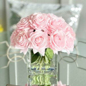 May include: A bouquet of pink silk roses arranged in a clear glass vase. The roses are in a round shape and the vase is square.