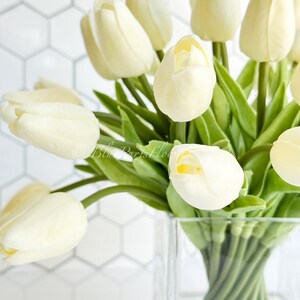 May include: A bouquet of white tulips arranged in a clear glass vase. The tulips are in a simple, modern style and would make a beautiful centerpiece for any home.