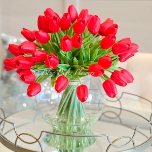 May include: A bouquet of red tulips arranged in a clear glass vase. The vase is sitting on a silver tray with a mirrored surface.