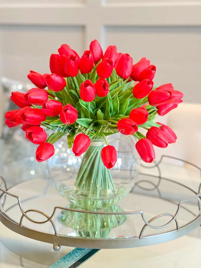 May include: A bouquet of red tulips arranged in a clear glass vase. The vase is sitting on a silver tray with a mirrored surface.