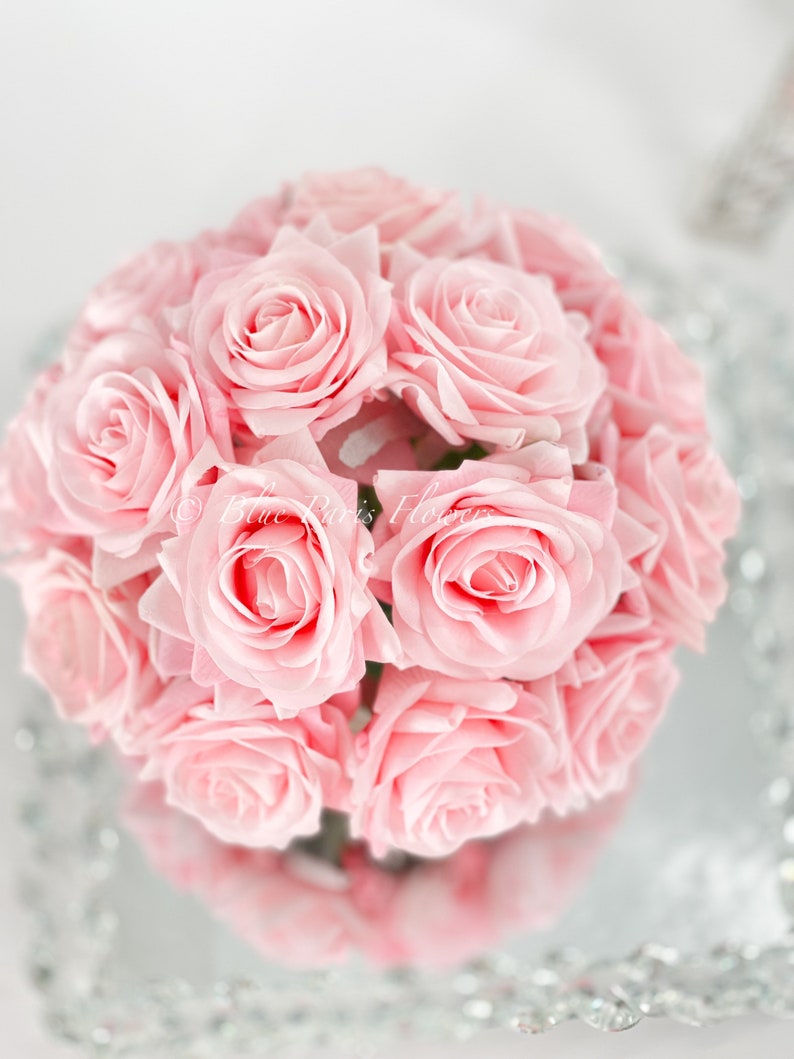 May include: A bouquet of pink roses arranged in a circular shape. The roses are tightly packed together, creating a full and lush appearance.