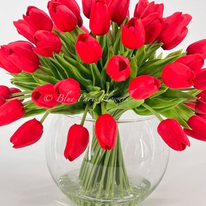 May include: A bouquet of red tulips arranged in a clear glass vase. The tulips are in full bloom and have green stems.