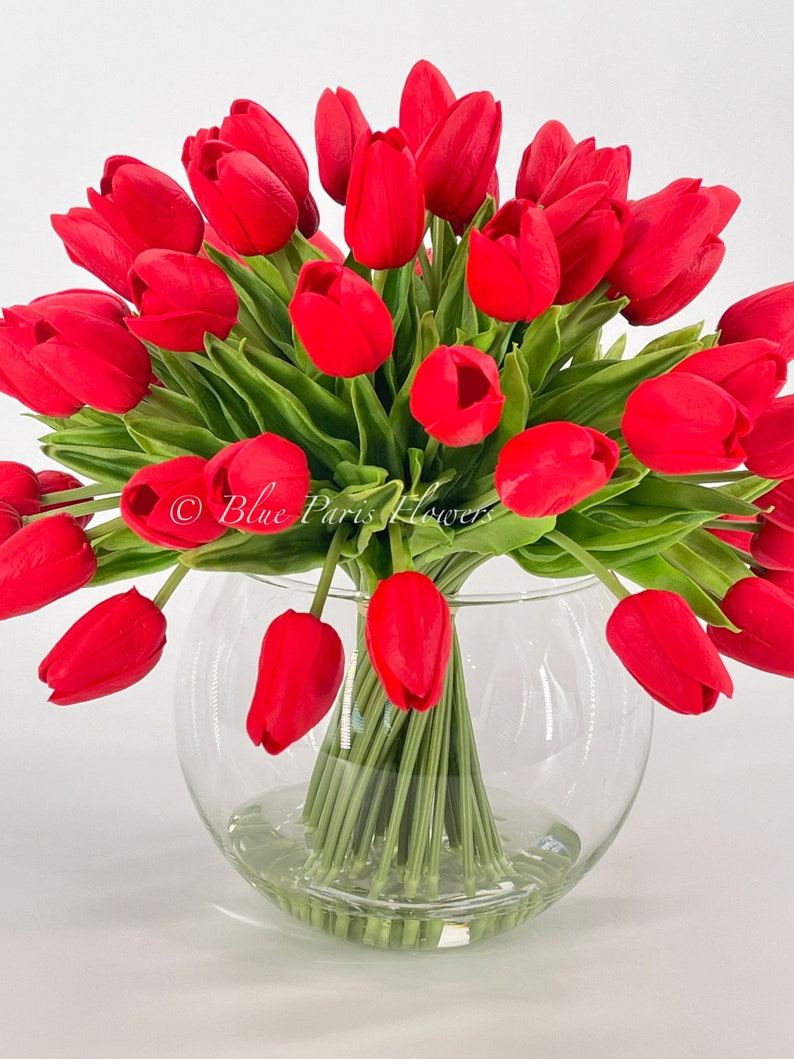May include: A bouquet of red tulips arranged in a clear glass vase. The tulips are in full bloom and have green stems.