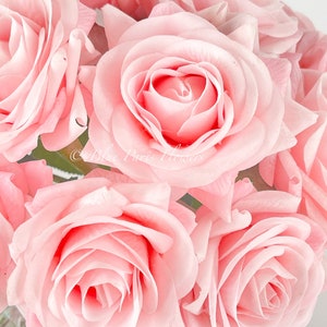 May include: A bouquet of pink silk roses in a clear glass vase. The roses are arranged in a circular pattern, with the stems facing outward.