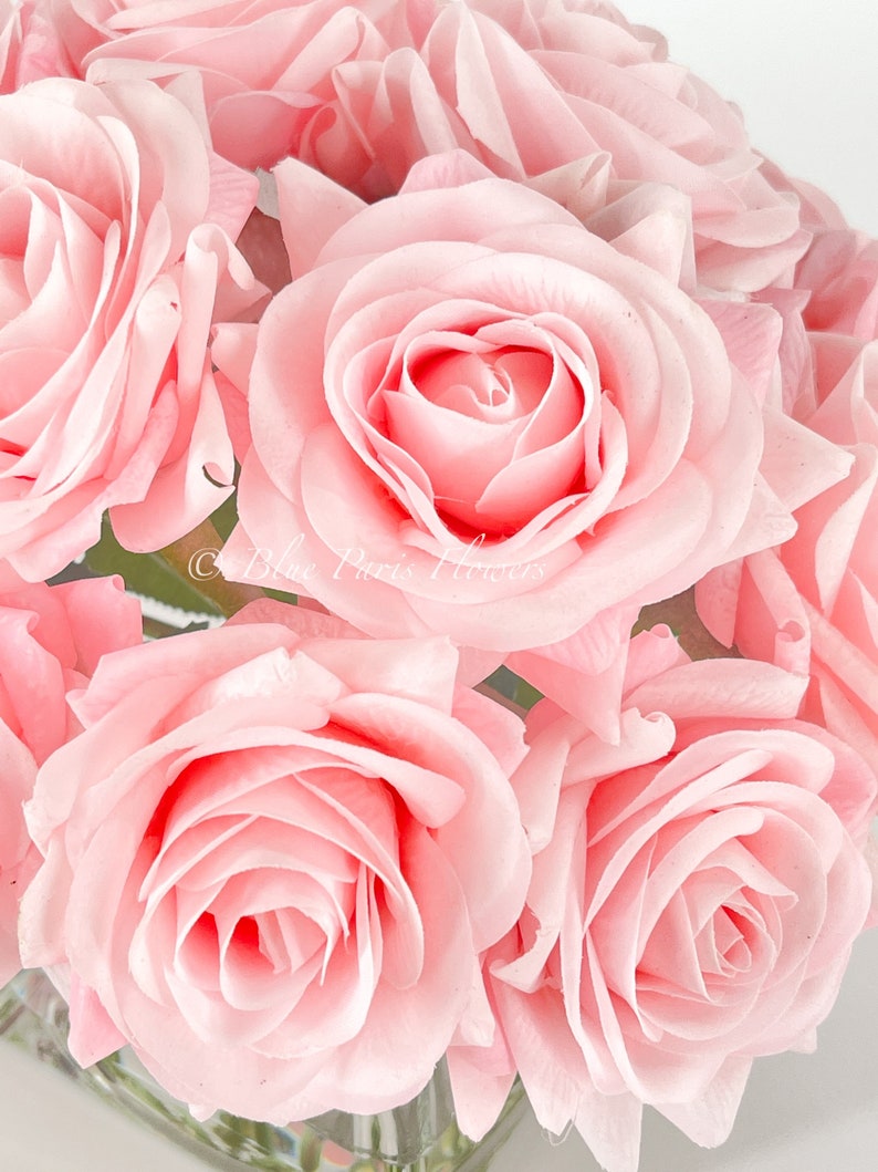 May include: A bouquet of pink silk roses in a clear glass vase. The roses are arranged in a circular pattern, with the stems facing outward.