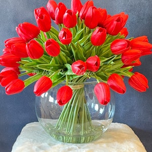 May include: A bouquet of red tulips arranged in a clear glass vase. The vase is sitting on a white fluffy surface.