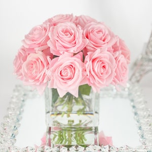 May include: A bouquet of pink roses in a clear glass vase, sitting on a mirrored tray with a crystal border.