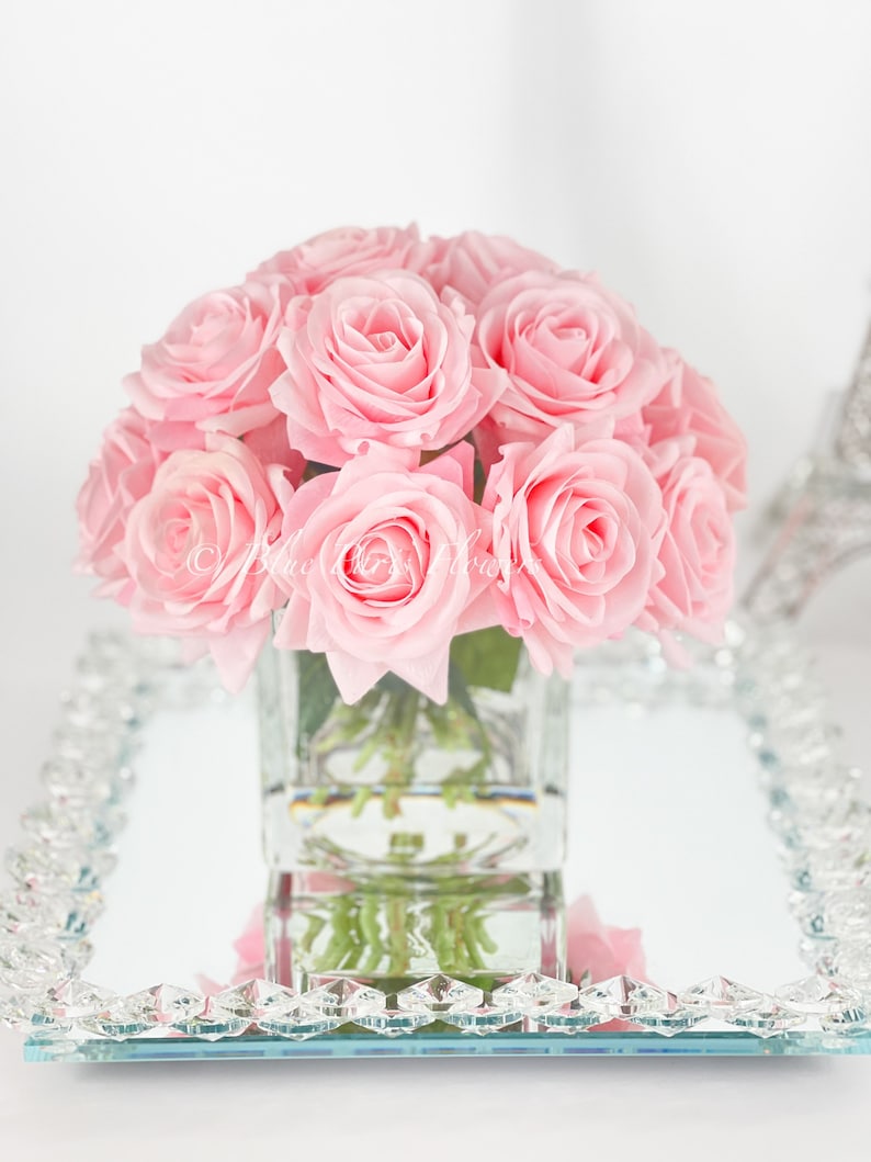 May include: A bouquet of pink roses in a clear glass vase, sitting on a mirrored tray with a crystal border.