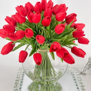 May include: A bouquet of red tulips arranged in a clear glass vase. The vase is sitting on a mirrored tray with a crystal-like border.