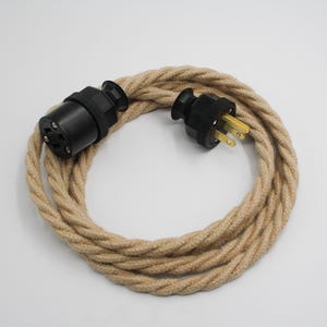 Peut inclure: Un cordon électrique recouvert de tissu beige avec une prise noire à chaque extrémité. Le cordon est enroulé en cercle.