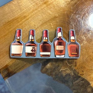 May include: A sticker featuring five brown liquor bottles with red wax seals. The bottles have white labels, with one labeled "No 46" and another "101". The sticker is on a wooden surface.