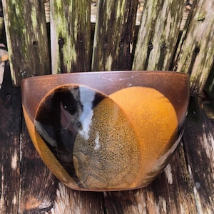 May include: A brown ceramic bowl with a black and yellow glaze. The bowl has a rounded shape and a wide rim.