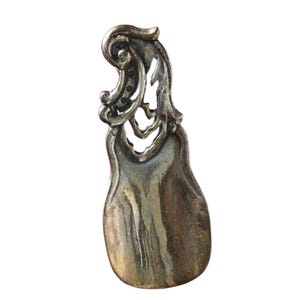 Puede incluir: Una cuchara de metal de color plateado con un mango adornado y decorativo. El mango tiene forma de rollo con detalles intrincados.