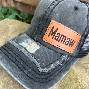 May include: A black distressed baseball cap with a brown leather patch that says "Mamaw" on it. The cap has a mesh back.