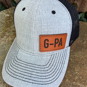 May include: A gray and black trucker hat with a brown leather patch that says "G-PA".