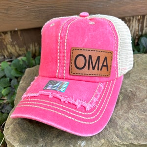 May include: Pink and beige distressed baseball cap with a brown leather patch that says "OMA" on it. The cap has a small American flag patch on the front.